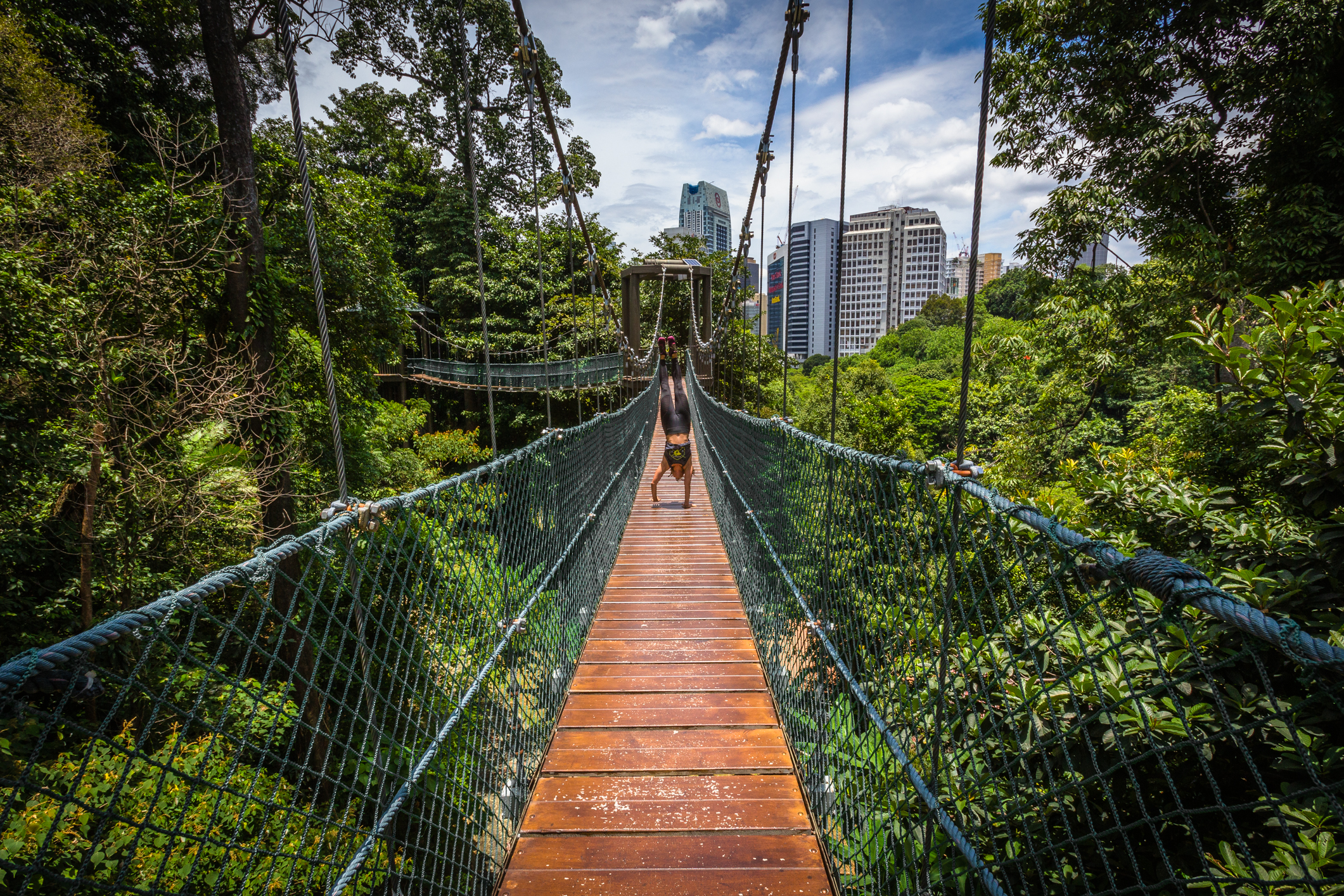 a girl standing on hands on a woodem bridge in a green city park
